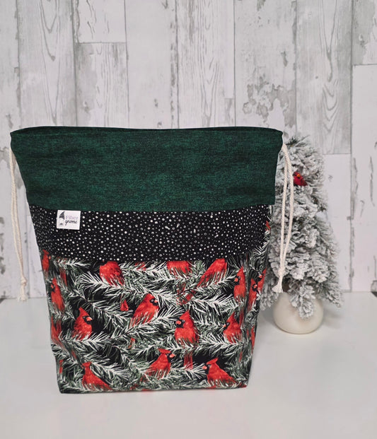 Green drawstring bag with red bird pattern on a snowy branches. Tree accent for scale and white wooden background.