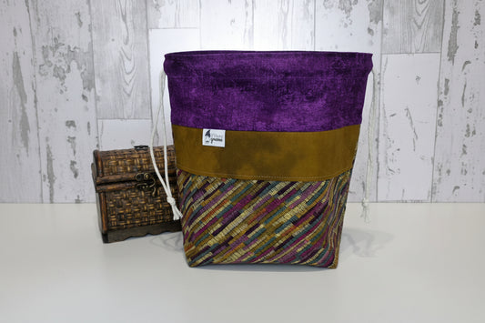 Fabric bag with purple top section and patterned bottom. With a wood accent for scale and a wooden background.